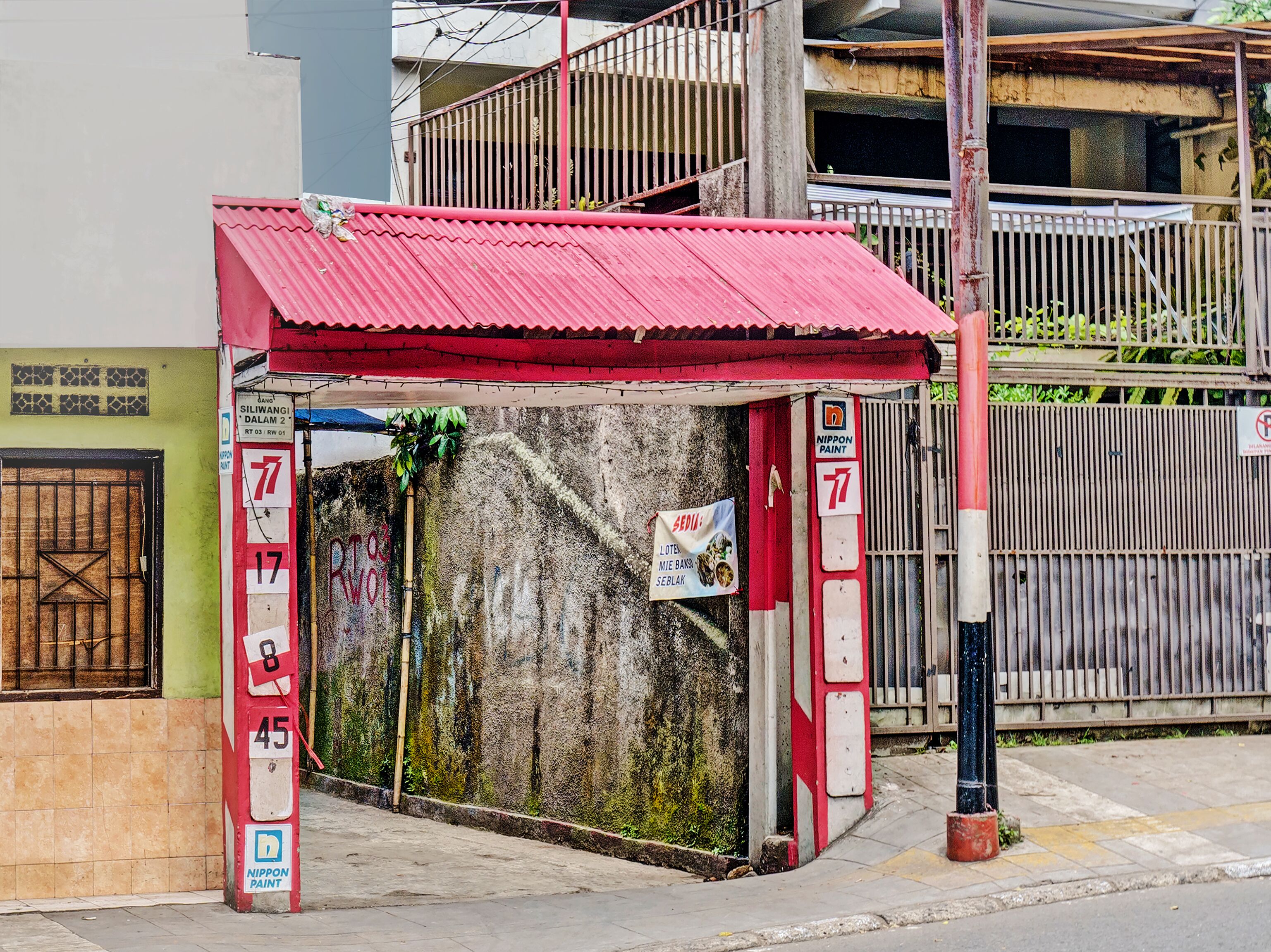 Een klein gebouwtje met een rood dak en een bord waarop staat dat het een Nippon Paint servicepunt is.