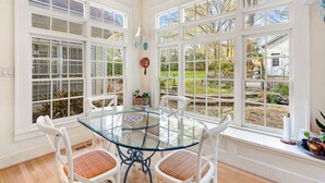 A dining area with a glass table and white chairs, large windows with blinds, and a view of the garden. - Walk to Town |Hot Tub |Chef Kitchen - The Sunny Spot (Decatur)