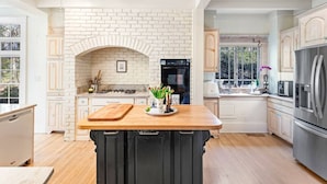 A kitchen with a brick wall, wooden cabinets, a central island, and modern appliances. - Walk to Town |Hot Tub |Chef Kitchen - The Sunny Spot (Decatur)