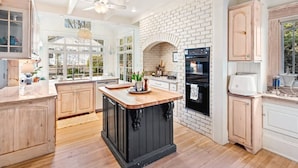 A kitchen with a central island, white brick walls, wooden cabinets, and a view of the outdoors. - Walk to Town |Hot Tub |Chef Kitchen - The Sunny Spot (Decatur)