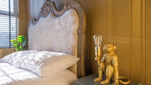 Een bed met wit beddengoed, een decoratief hoofdbord en een gouden beeldje op een nachtkastje.