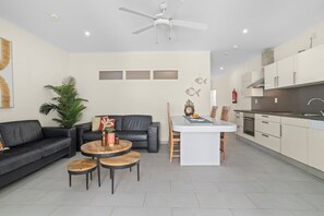 A modern kitchen with white cabinets, a central island, and a dining area with a black leather couch and wooden tables.