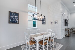 A dining area with a white table and chairs, a hanging light fixture, and artwork on the walls.