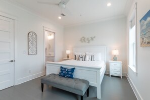 A bedroom with a large bed, bedside tables, a bench, and a ceiling fan.