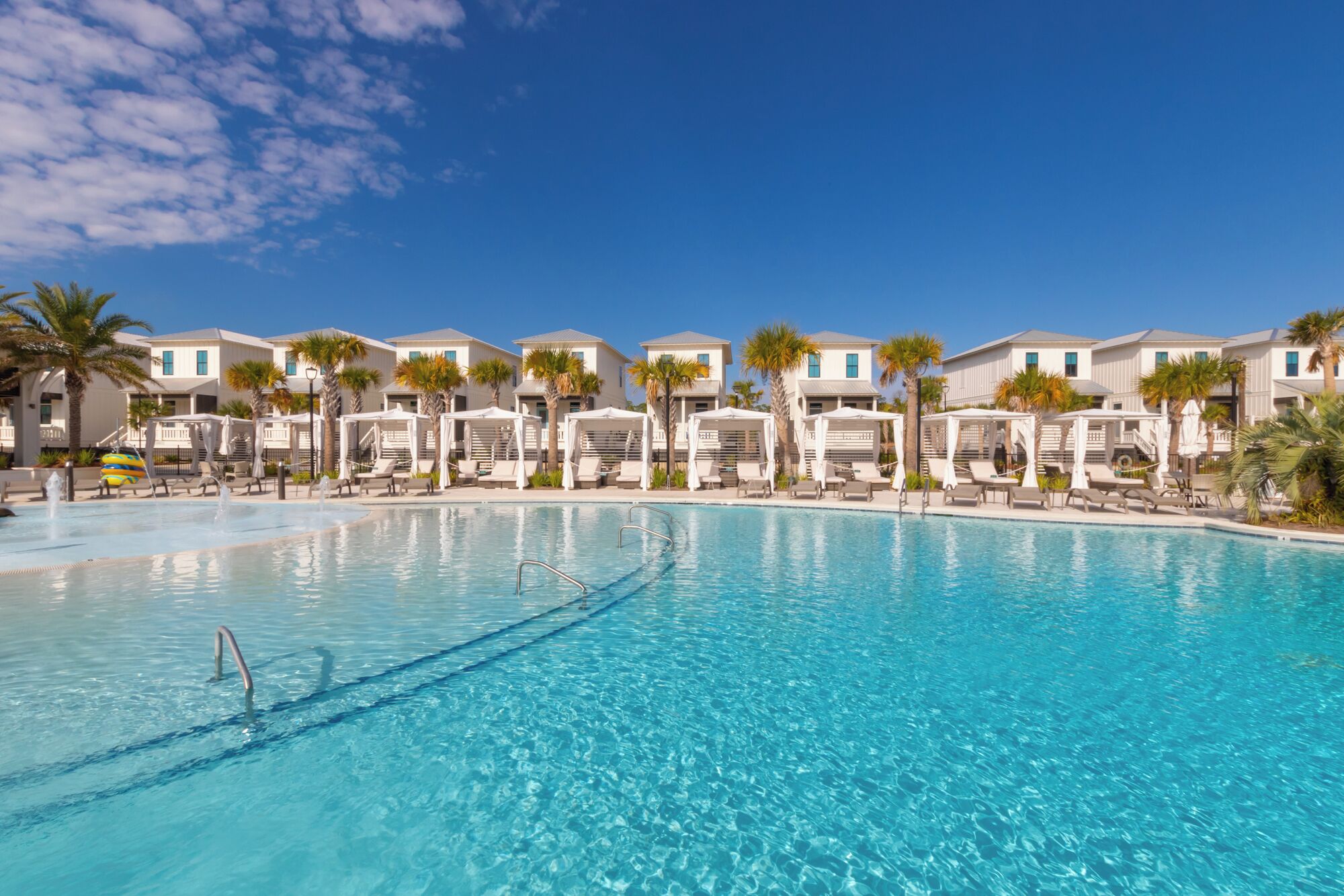 A swimming pool with lounge chairs and umbrellas, surrounded by buildings with a uniform architectural style.