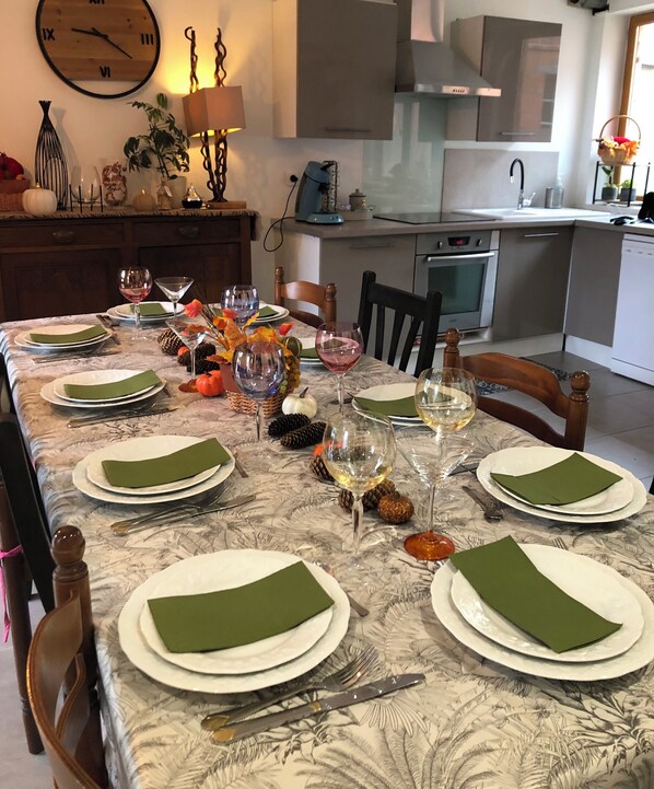 Mesa de comedor preparada para seis personas, con servilletas verdes, platos blancos y copas de vino.