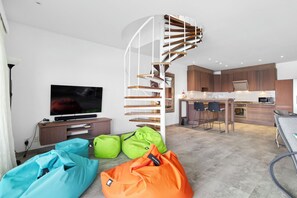 A modern apartment with a spiral staircase, a kitchen, a dining area, and a living room with bean bags.