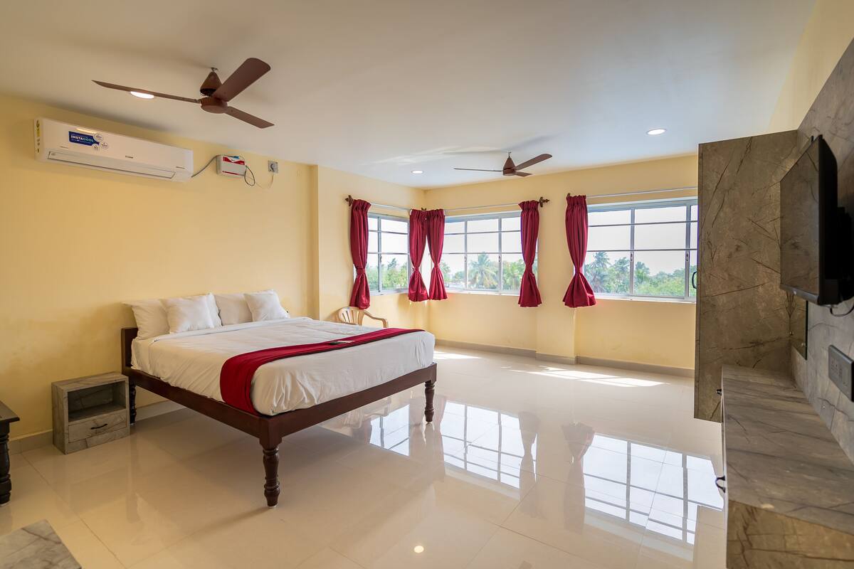 Un dormitorio amplio con una cama grande, dos ventiladores de techo, una ventana con cortinas rojas y una chimenea de mármol.