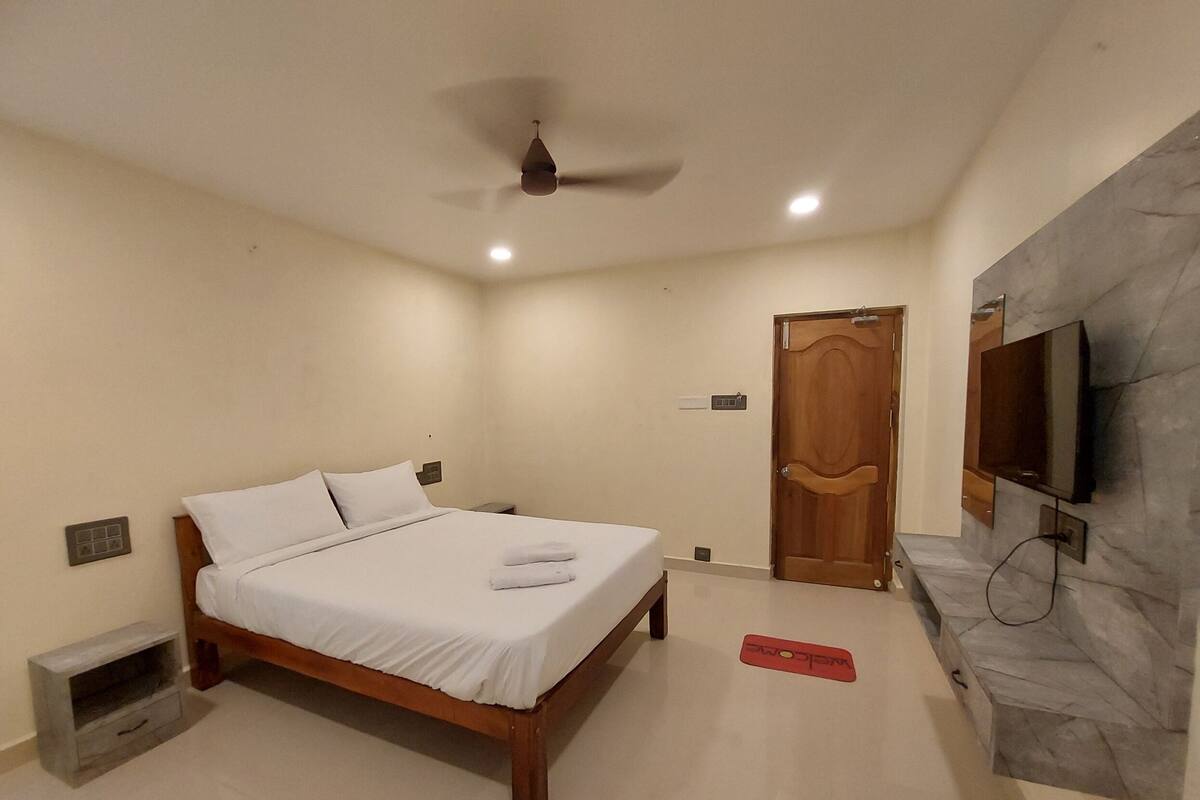 Un dormitorio con cama, ventilador de techo, televisor montado en la pared y puerta de madera.