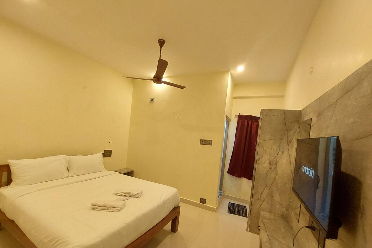Una habitación de hotel con cama, ventilador de techo, televisor montado en la pared y pared con textura de mármol.