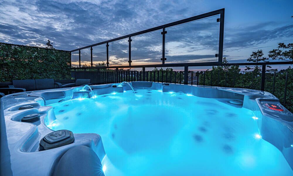 Ein Whirlpool mit Glasabdeckung, umgeben von Sitzgelegenheiten im Freien und Blick auf den Himmel.