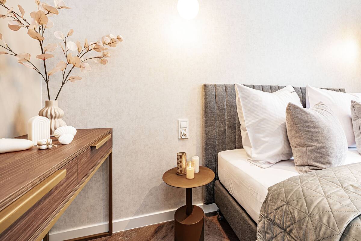 Een moderne slaapkamer met een bed, nachtkastje en een klein bijzettafeltje met decoratieve objecten.