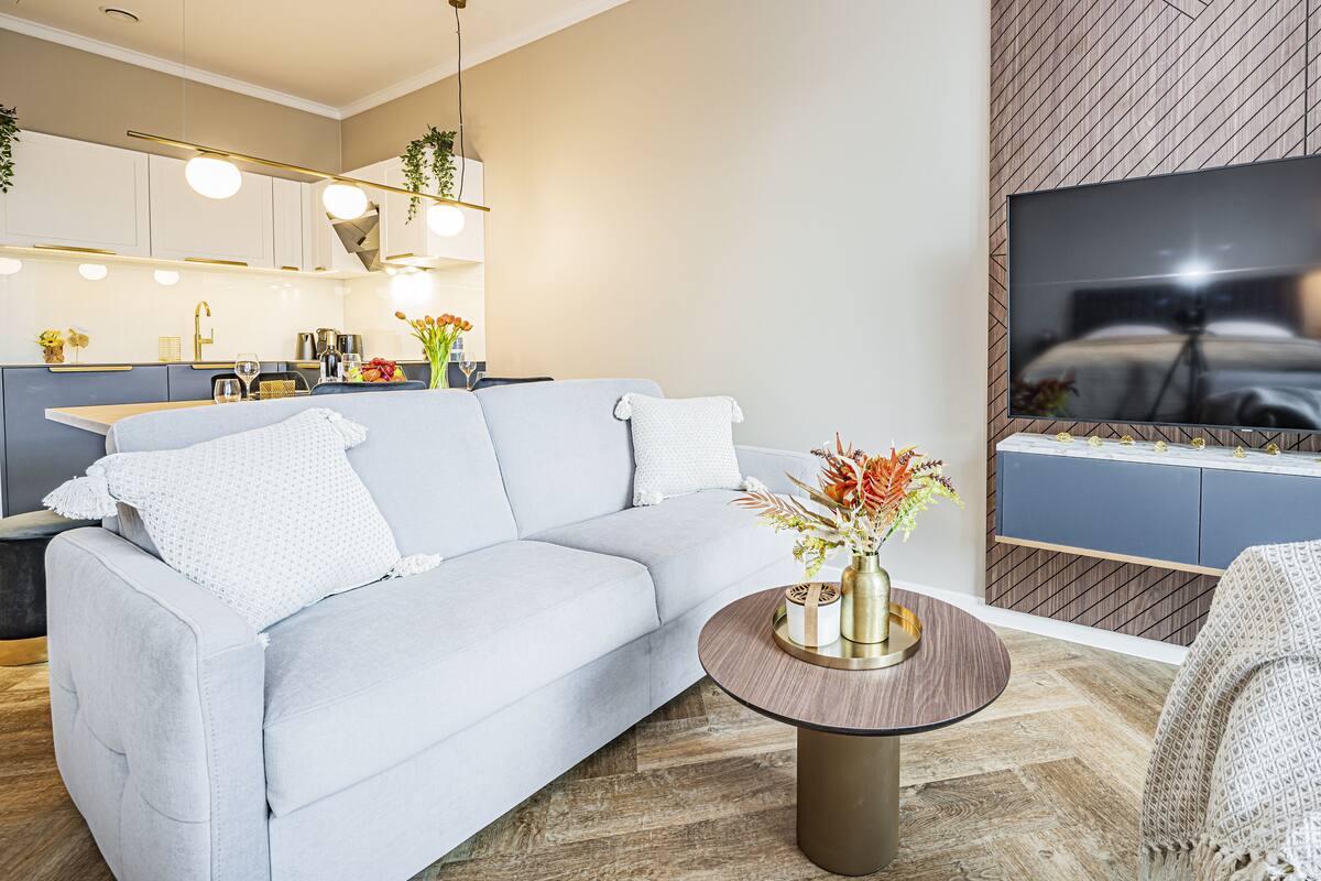 Een moderne woonkamer met een bank, een ronde salontafel en een aan de muur bevestigde televisie.