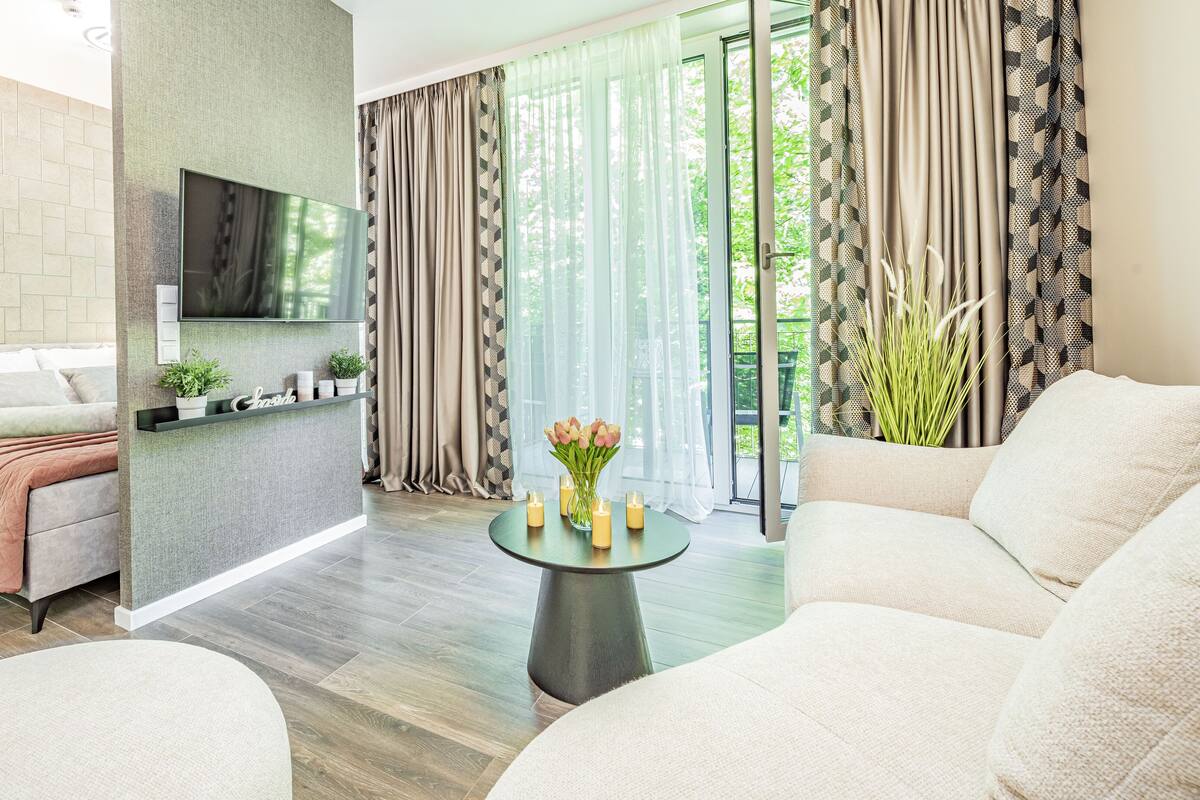 Een moderne woonkamer met een bank, een salontafel met kaarsen, en een aan de muur bevestigde televisie.