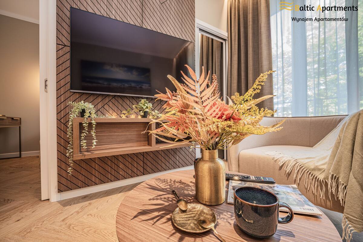Een moderne woonkamer met een flatscreen televisie bevestigd aan een houten wand, een ronde salontafel met een vaas gedroogde bloemen, een tijdschrift en een mok.