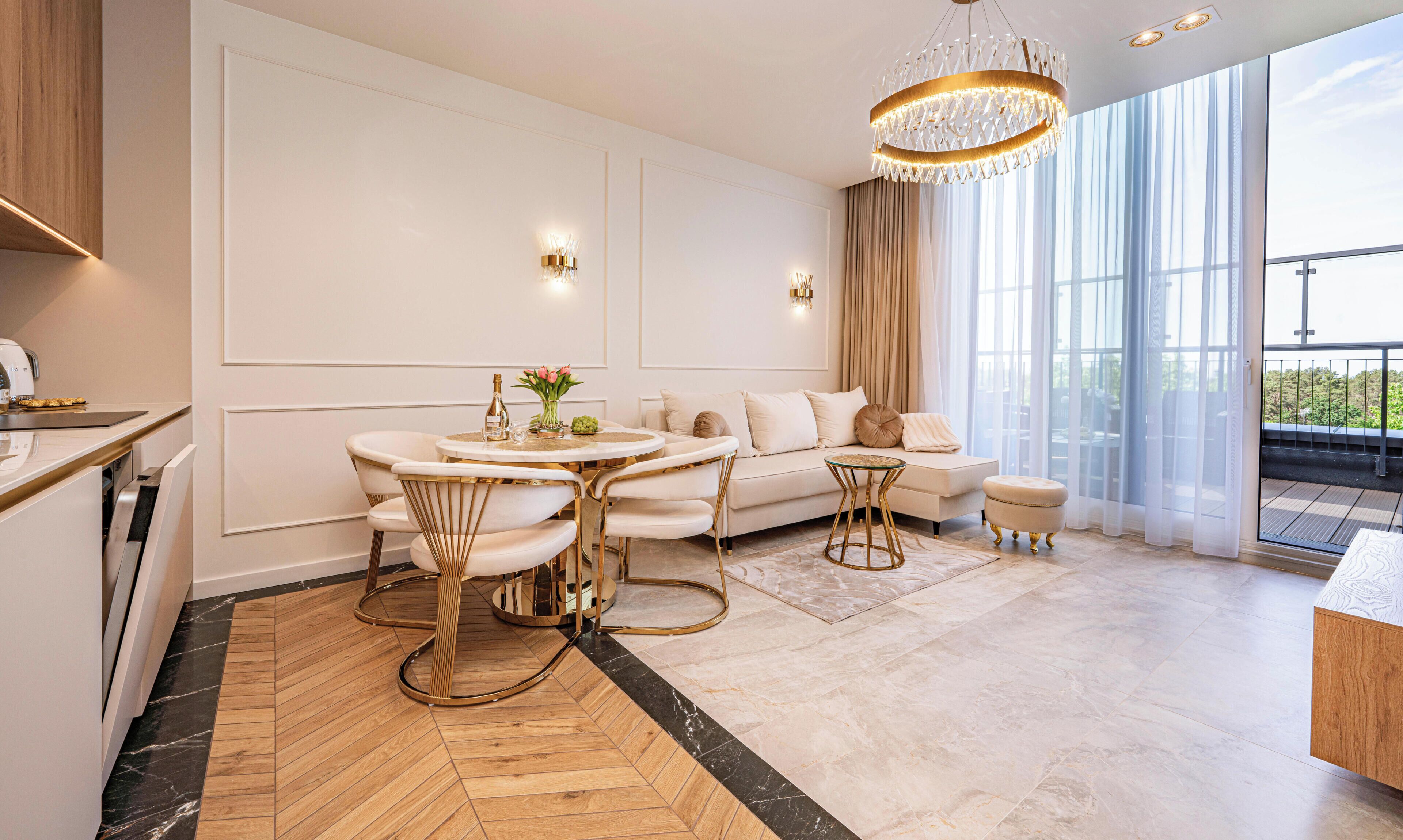 Un salon moderne avec une table à manger ronde, un canapé et un pouf, un lustre et une grande fenêtre offrant une belle vue.