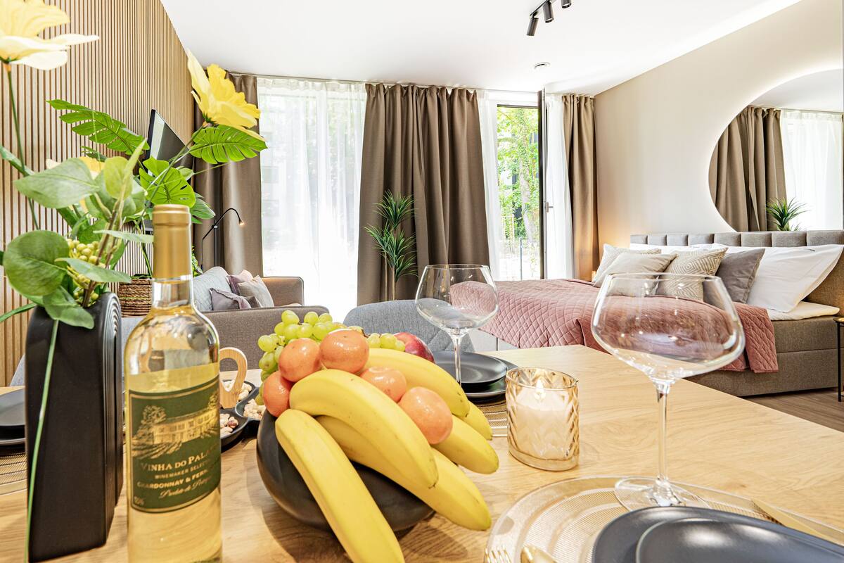 Een eettafel met een fles wijn, een schaal fruit en wijnglazen.