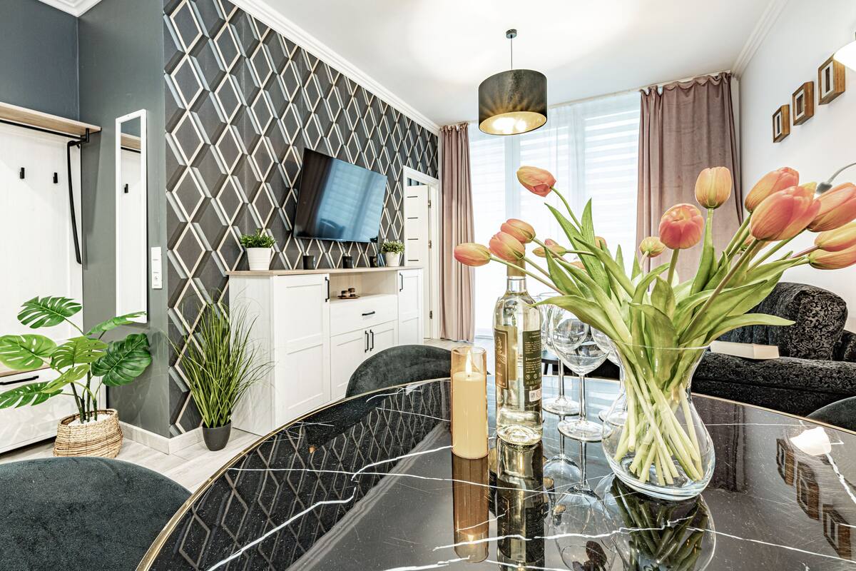 Een moderne woonkamer met een zwarte marmeren eettafel, een flatscreen televisie aan de muur en een vaas met roze tulpen.
