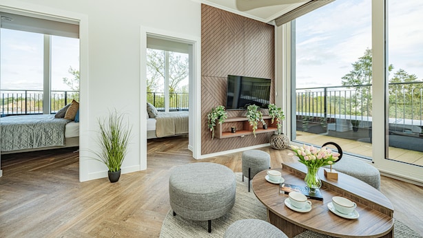 A modern living room with a large TV, comfortable seating, and a balcony with a view.