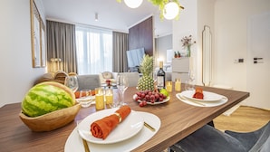 A dining area with a wooden table set for two, featuring a watermelon bowl, plates, cutlery, and candles.