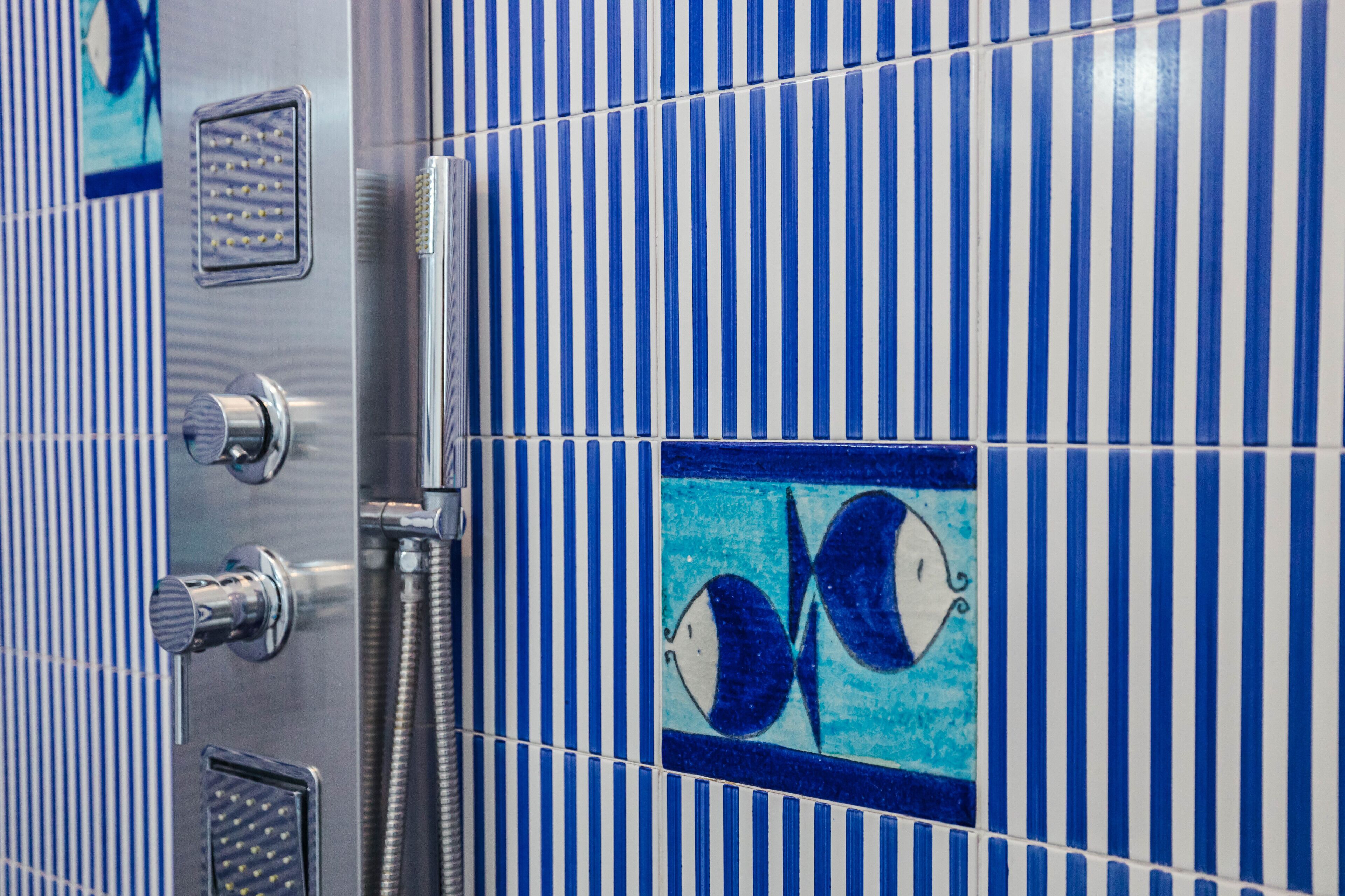 A bathroom with blue and white striped tiles, a shower with a chrome faucet, and a decorative tile with a fish design.