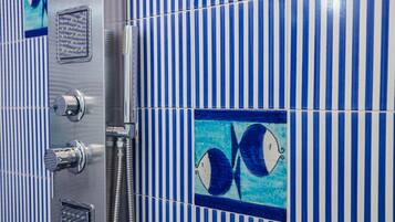 A bathroom with blue and white striped tiles, a shower with a chrome faucet, and a decorative tile with a fish design.