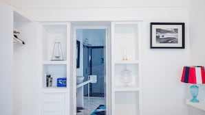 A hallway with a white door leading to a bathroom with a blue and white tiled floor. Shelves on either side of the hallway contain various items, including a lamp and a framed picture. - Boutique Suite in Piazzetta (Capri)