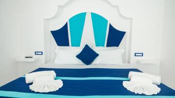 A hotel room with a large bed, white headboard, and blue bedding. There are two bedside tables with lamps and a power outlet on each.