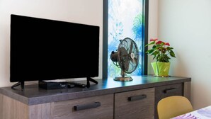 A room with a TV on a desk, a standing fan, a potted plant, and a chair. - Appartementmaïthé 3 (Saint-Paul)