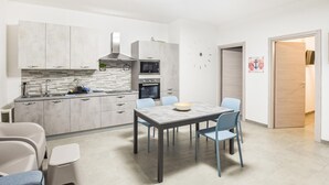 A modern kitchen with grey cabinets, a built-in oven, and a microwave. There is a dining table with chairs and a bowl on it. - Lovely home in Marina di Ragusa (Marina di Ragusa)