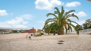 A rooftop terrace with stone flooring, a palm tree, and a view of a town in the background. - Lovely home in Marina di Ragusa (Marina di Ragusa)