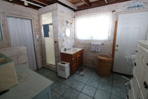 Een kleine badkamer met houten inrichting, een wastafel, een spiegel, een ventilator en een deur met een bordje.