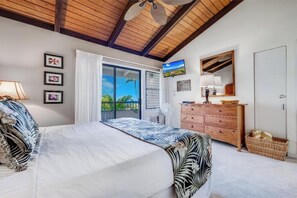 A bedroom with a bed, a dresser, a fan, and a window with a view of greenery.