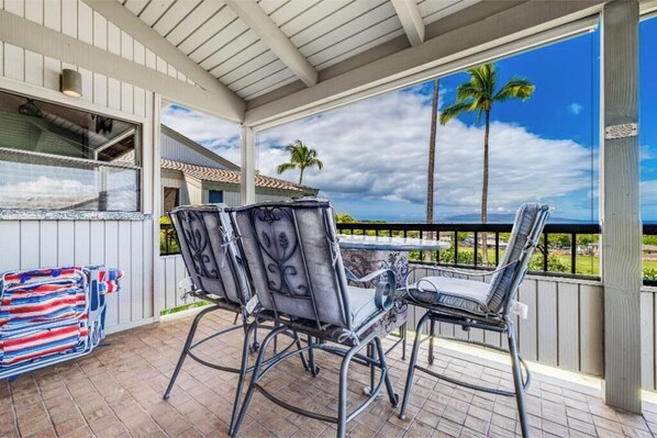 A covered outdoor patio with metal chairs and a table, overlooking a scenic view with palm trees and mountains.
