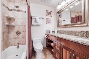 Une salle de bain équipée d’une baignoire, de toilettes, d’un meuble-lavabo avec un évier et d’un grand miroir.