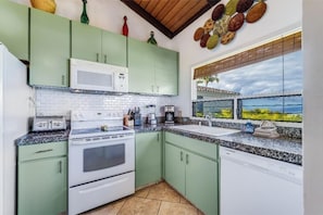 A kitchen with green cabinets, white appliances, and a window with a view of palm trees.