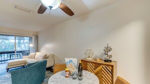 A modern living room with a white sofa, teal armchair, and a wooden cabinet with a geometric design. A round table with a marble top is in the center, surrounded by chairs. - Quaint Sarasota Condo: 4 Mi to Siesta Key Beach! (Sarasota)