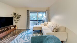 A living room with a flat-screen TV, a sofa, a coffee table, and a large window with curtains. - Quaint Sarasota Condo: 4 Mi to Siesta Key Beach! (Sarasota)