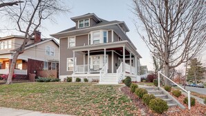 A two-story house with a front porch, a covered entryway, and a small front yard with a lawn and leaf-covered ground. - Charming Cincinnati Home w/ Spacious Deck! (Cincinnati)