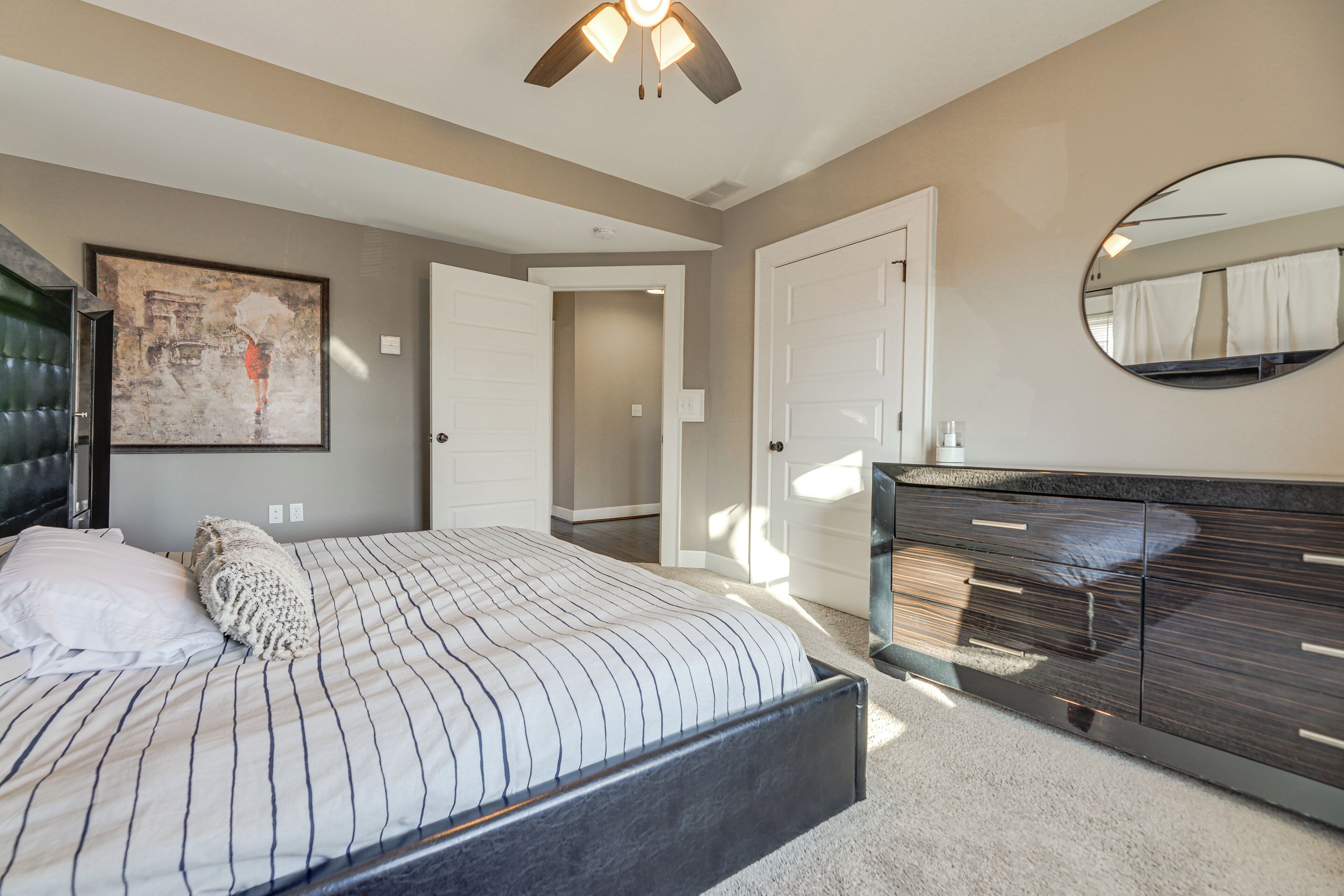 Un dormitorio con cama, cómoda, espejo y puerta que da a otra habitación.