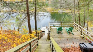 A wooden deck with chairs and a table overlooking a lake, surrounded by autumn foliage. - Great Barrington Lakeside Getaway w/ Kayak & Grill (Great Barrington)