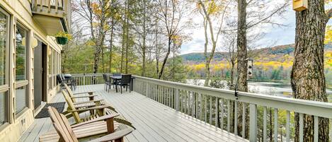 A wooden deck with outdoor seating, overlooking a river and autumn foliage.