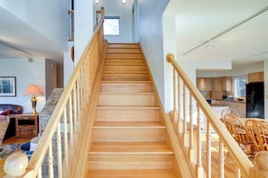 A staircase with wooden steps and a handrail, leading to a kitchen area with wooden cabinets and a dining table. - Great Barrington Lakeside Getaway w/ Kayak & Grill (Great Barrington)
