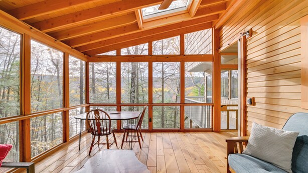 A wooden cabin with a large glass windowed porch, a dining table with chairs, and a sofa. - Great Barrington Lakeside Getaway w/ Kayak & Grill (Great Barrington)