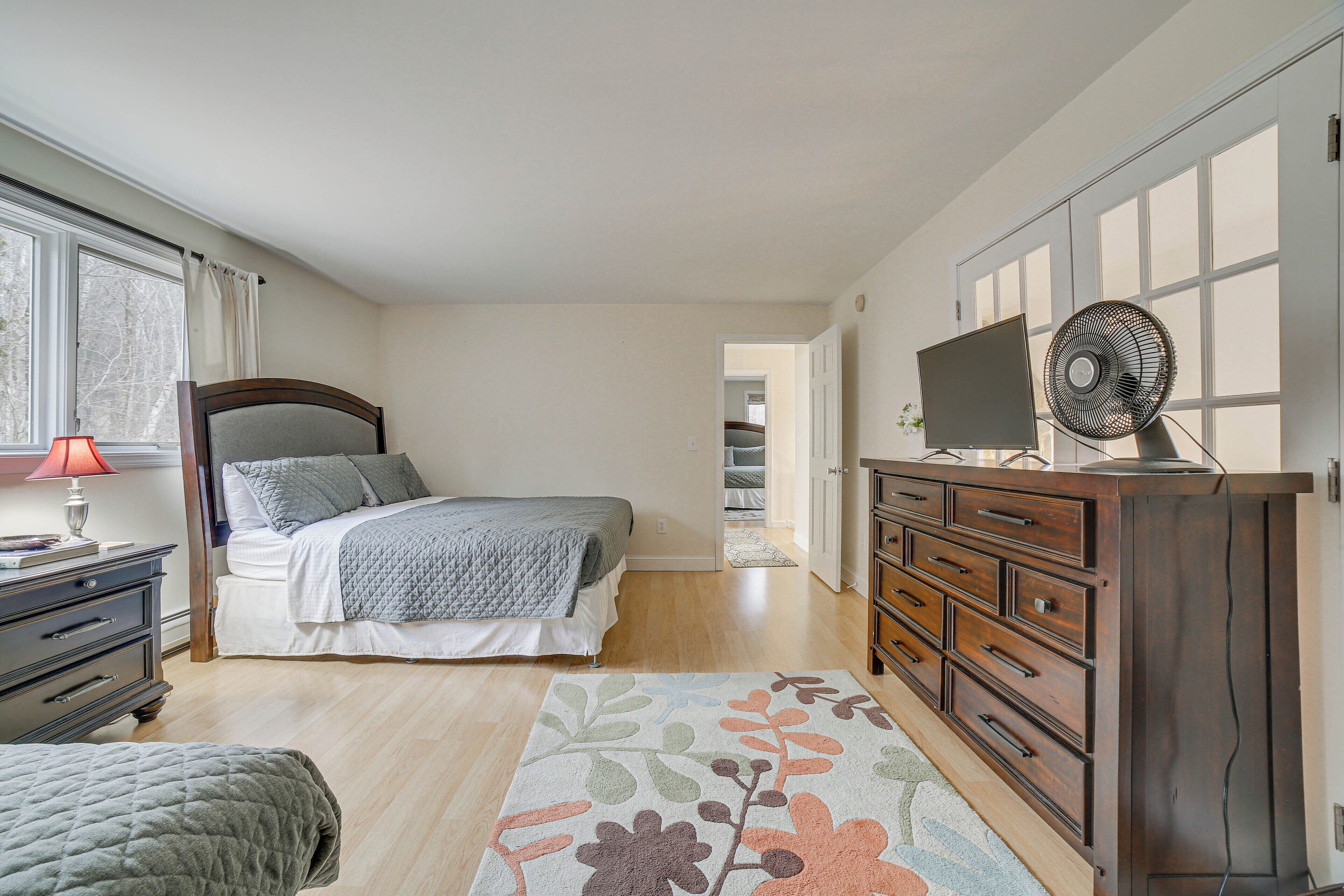 A bedroom with a bed, dresser, TV, and a window.
