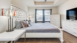 Une chambre à coucher comprenant un lit, des tables de chevet, un ventilateur de plafond, une commode et un téléviseur.
