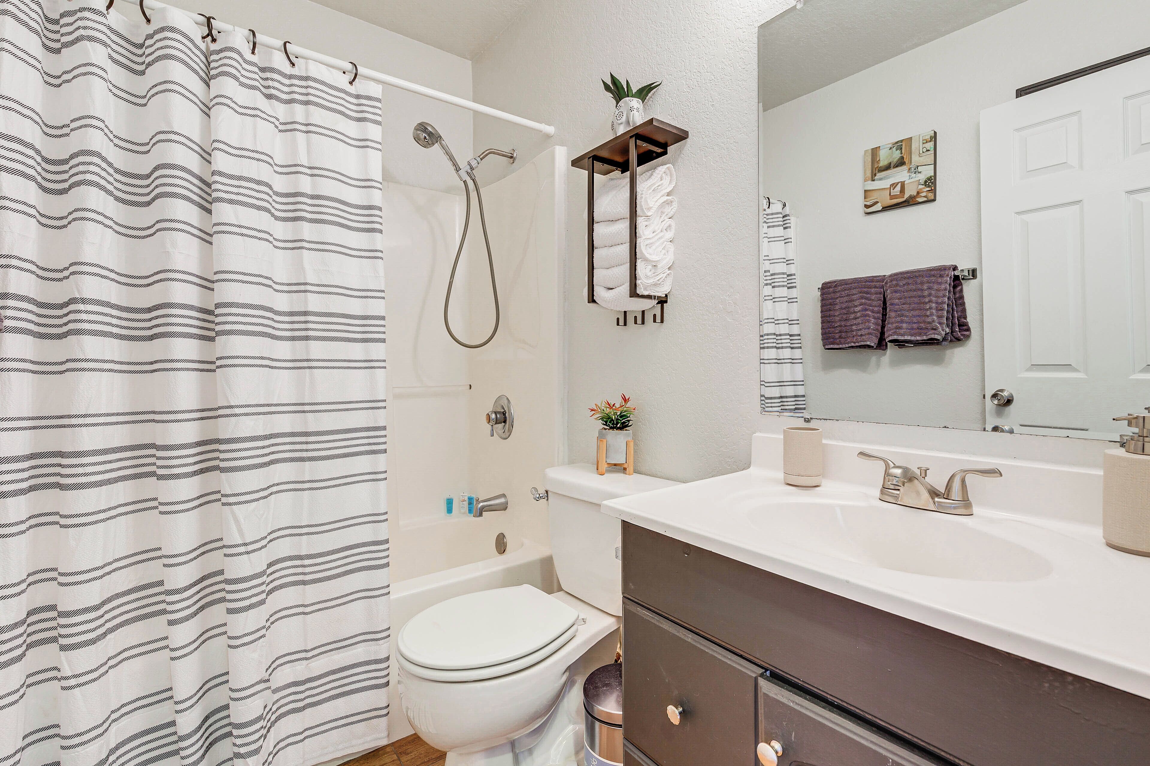 A bathroom with a shower curtain, a toilet, a sink, and a mirror.