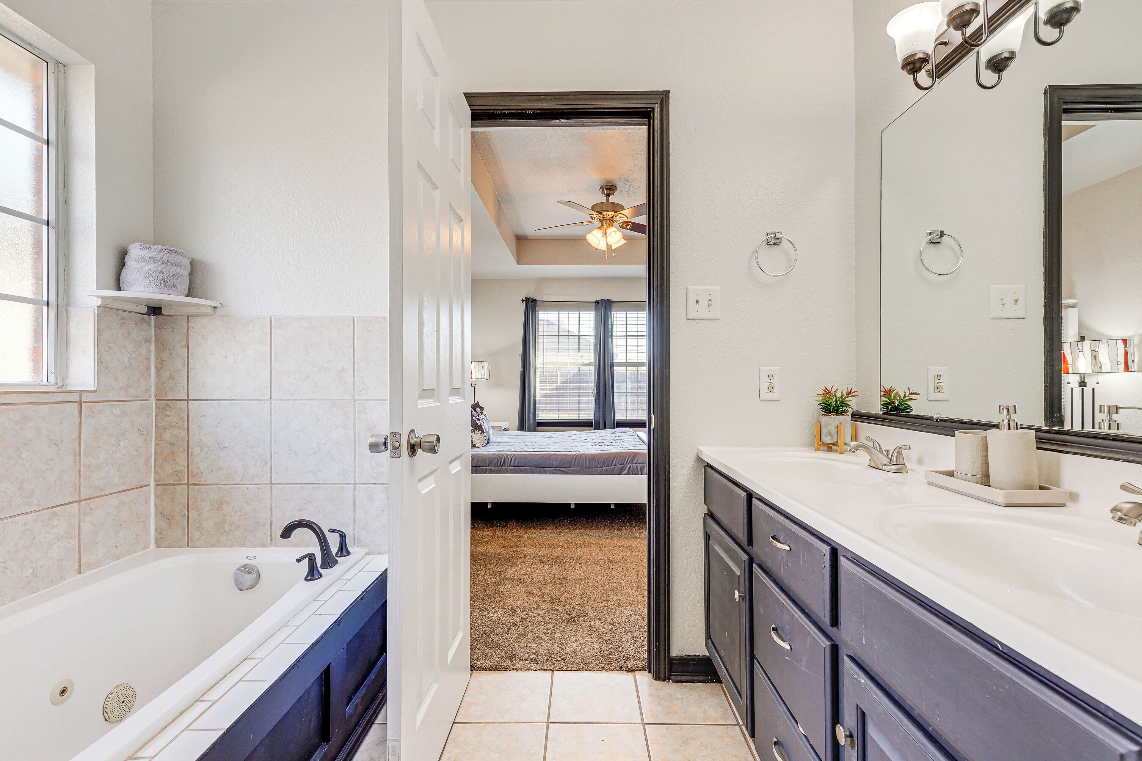 A modern bathroom with a bathtub, vanity, and a ceiling fan.