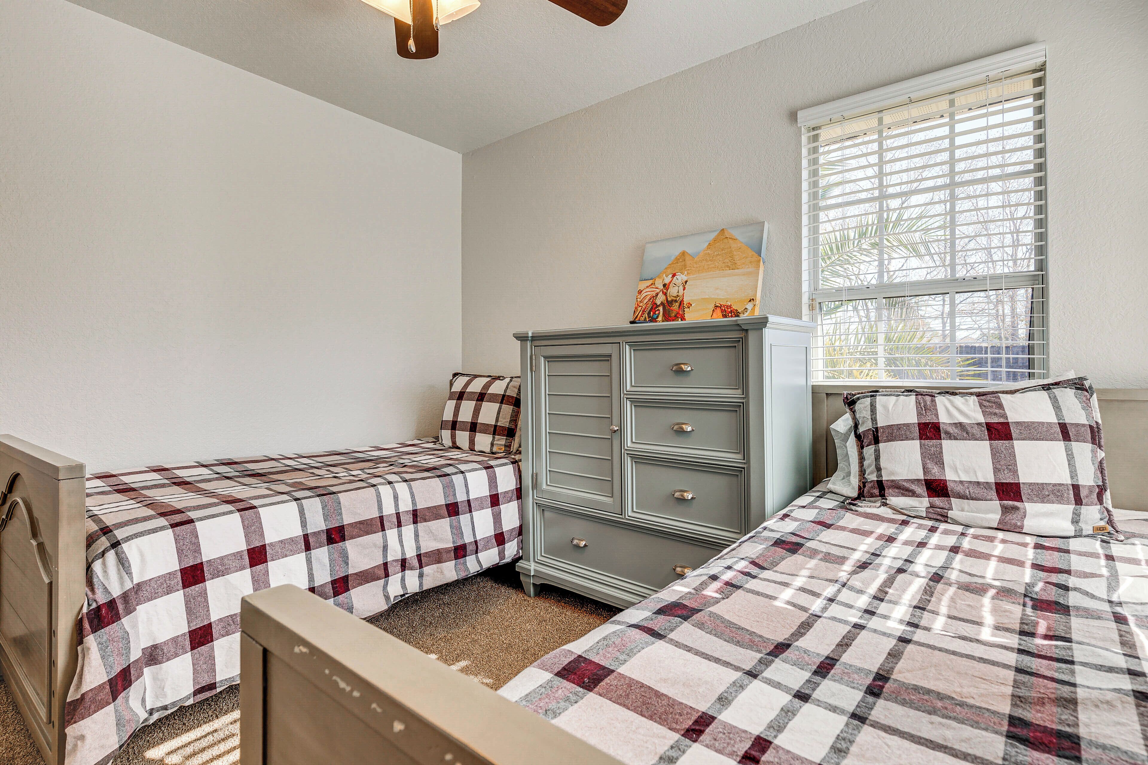 Een slaapkamer met twee bedden, een dressoir en een raam met jaloezieën.