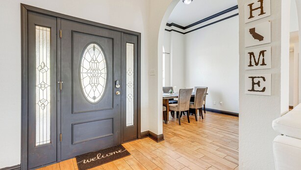 Une porte en bois sombre avec un panneau de verre, un paillasson et un coin repas avec des chaises et une table.